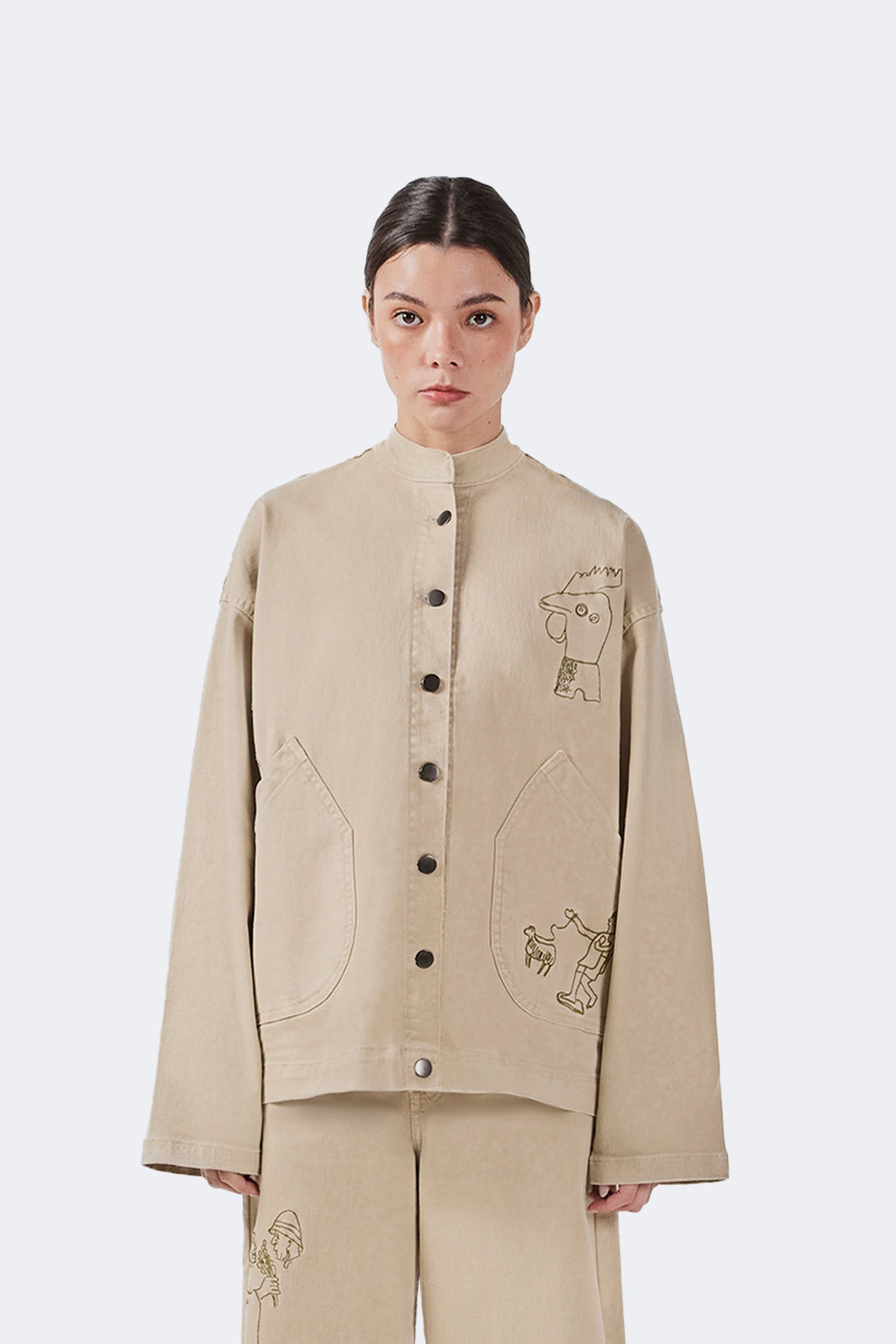 Close-up front detail of the Allpa Mandarin Jacket in Cream highlighting archive-inspired embroidery, snap-button closure, and oversized patch pockets.