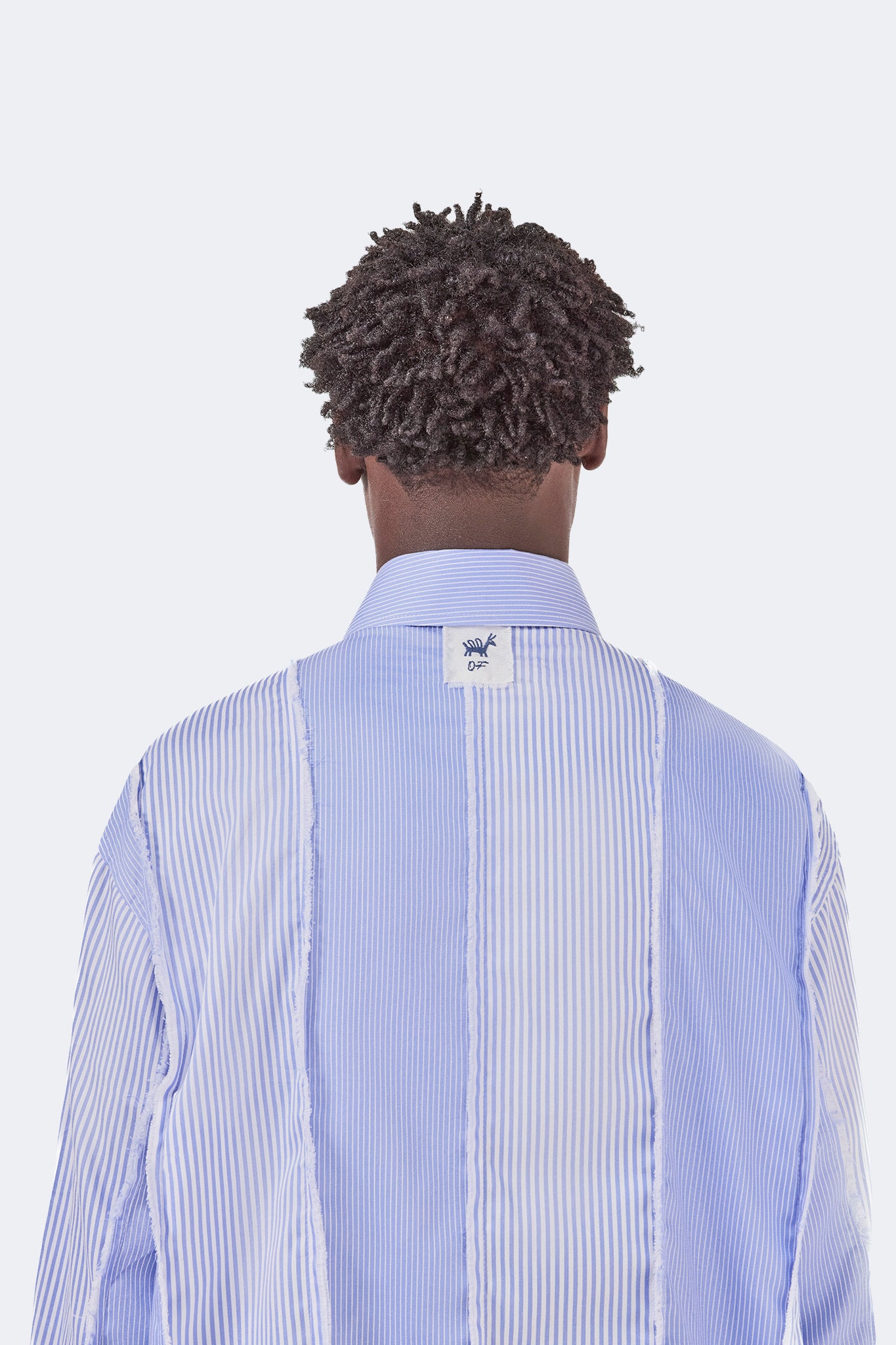 Close-up back view of the Canoa Blue Striped Cotton Shirt highlighting the collar, signature label, and exposed raw-edge panel construction.