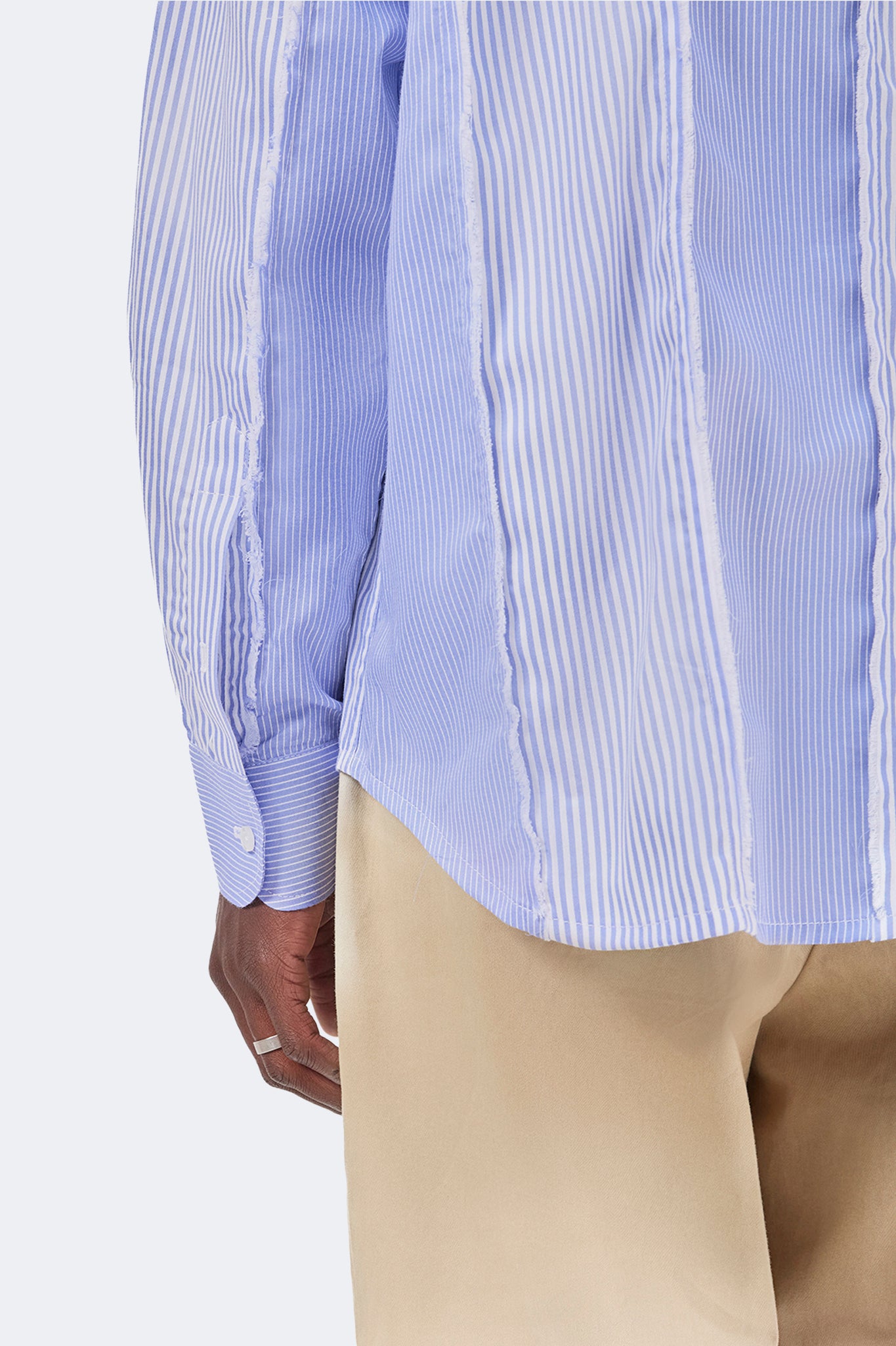 Detail of the back hem and sleeve of the Canoa Blue Striped Shirt showcasing raw-edge seams and striped panel construction.