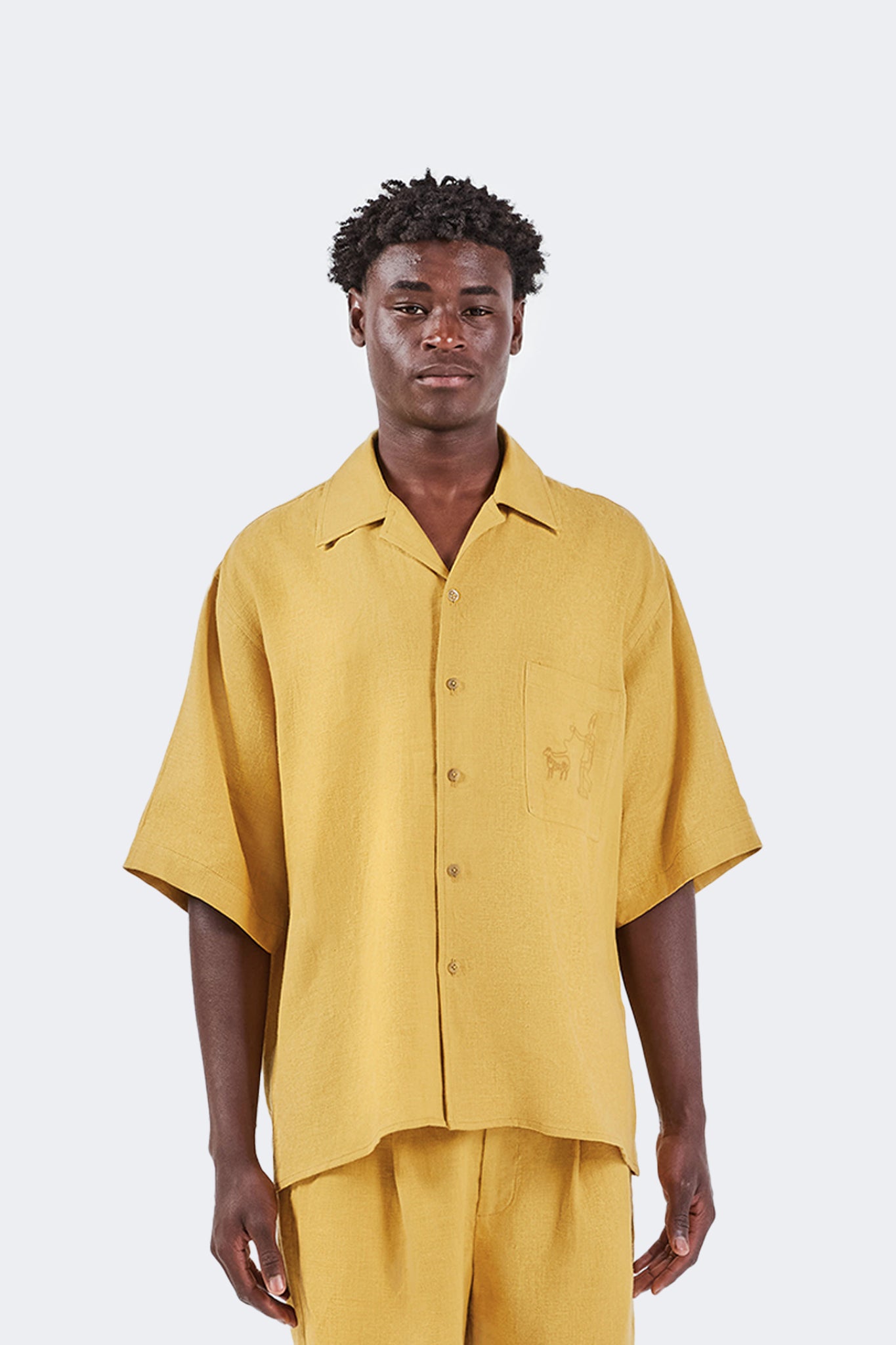 Close-up of the Floreana Short-Sleeved Shirt in Mustard featuring the embroidered chest pocket, open collar, and natural 100% linen texture.