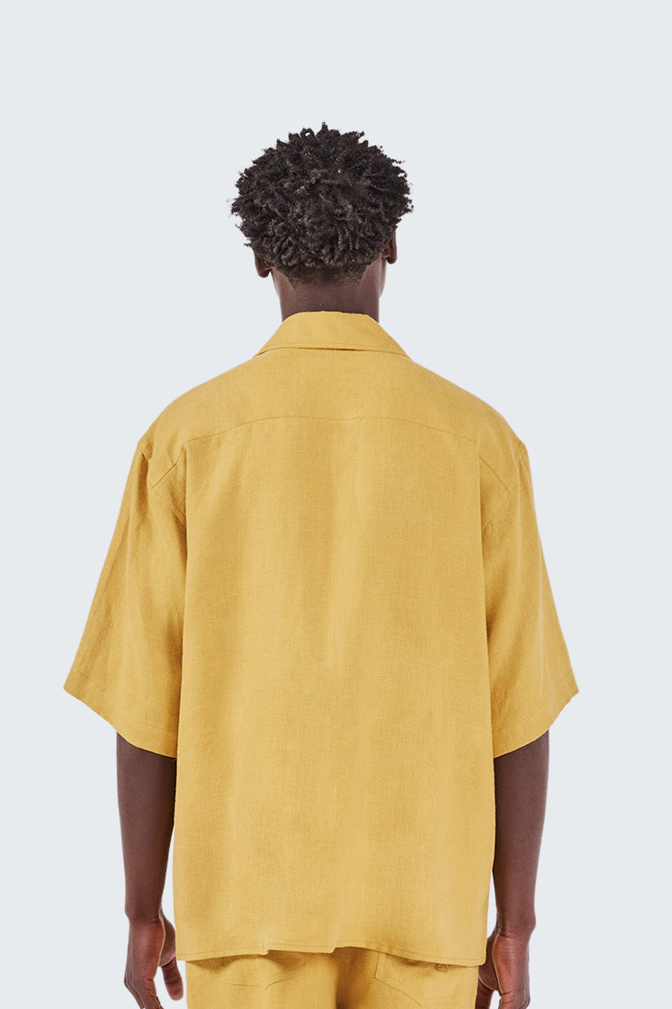 Person wearing a mustard yellow shirt and pants on a light gray background