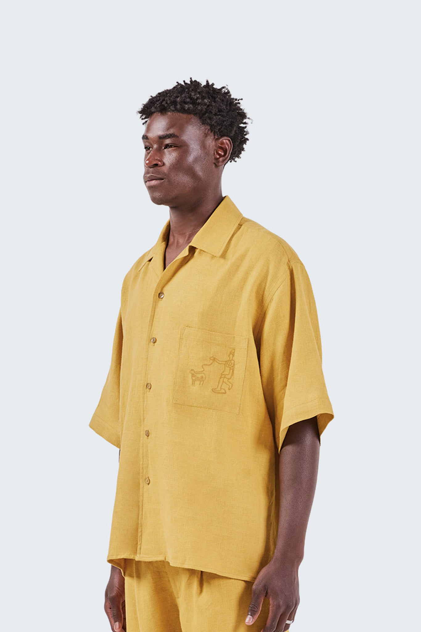 Man wearing a mustard yellow shirt with a small logo on a white background