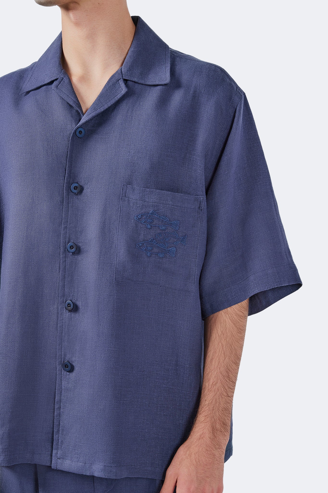 Close-up of the Isabela Blue Linen Short-Sleeved Shirt featuring tonal embroidered fish motif on the chest pocket.