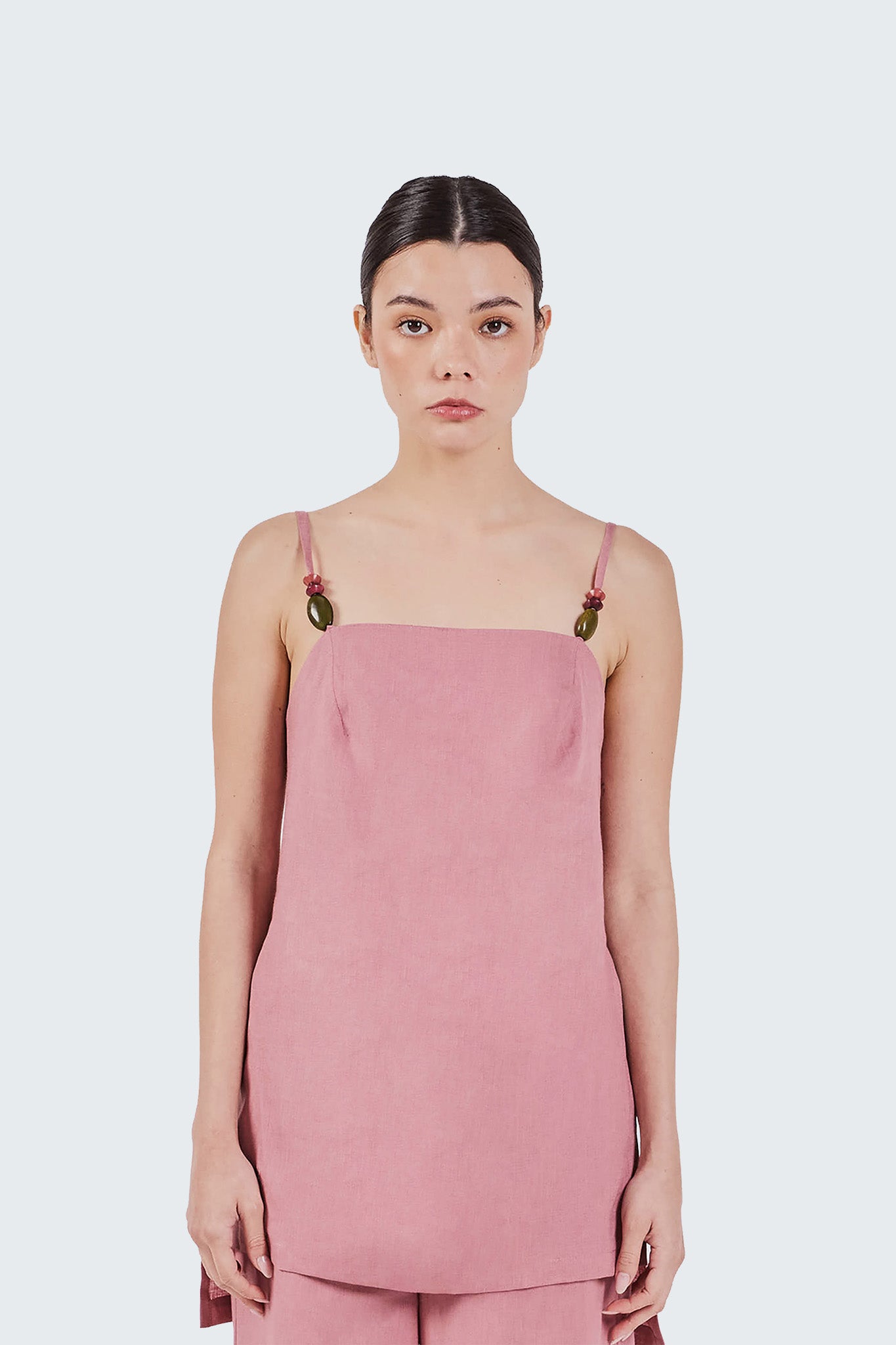 Woman wearing a pink Jama linen blouse with thin straps on a white background