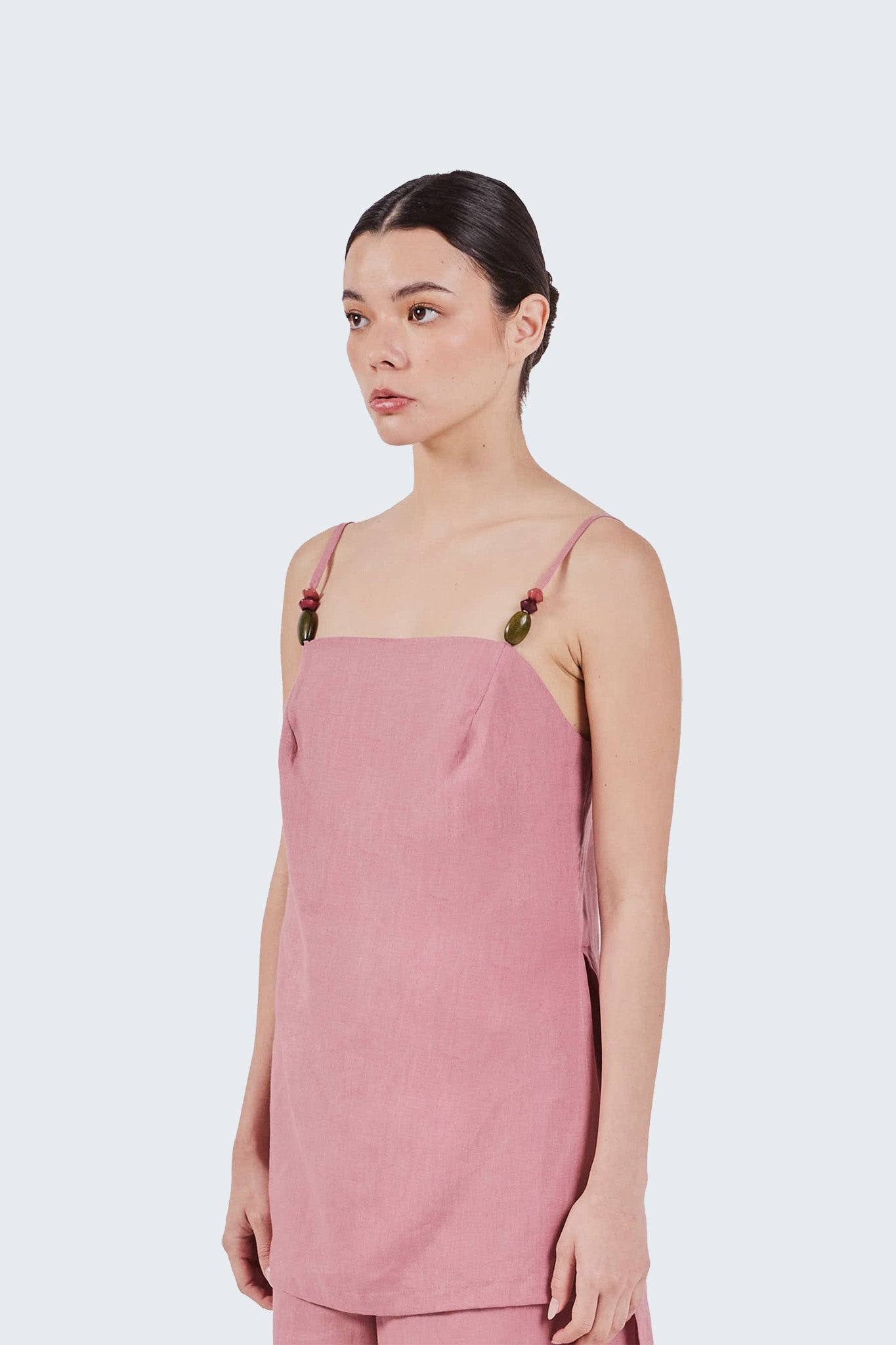 Woman wearing a pink sleeveless top with thin straps on a white background