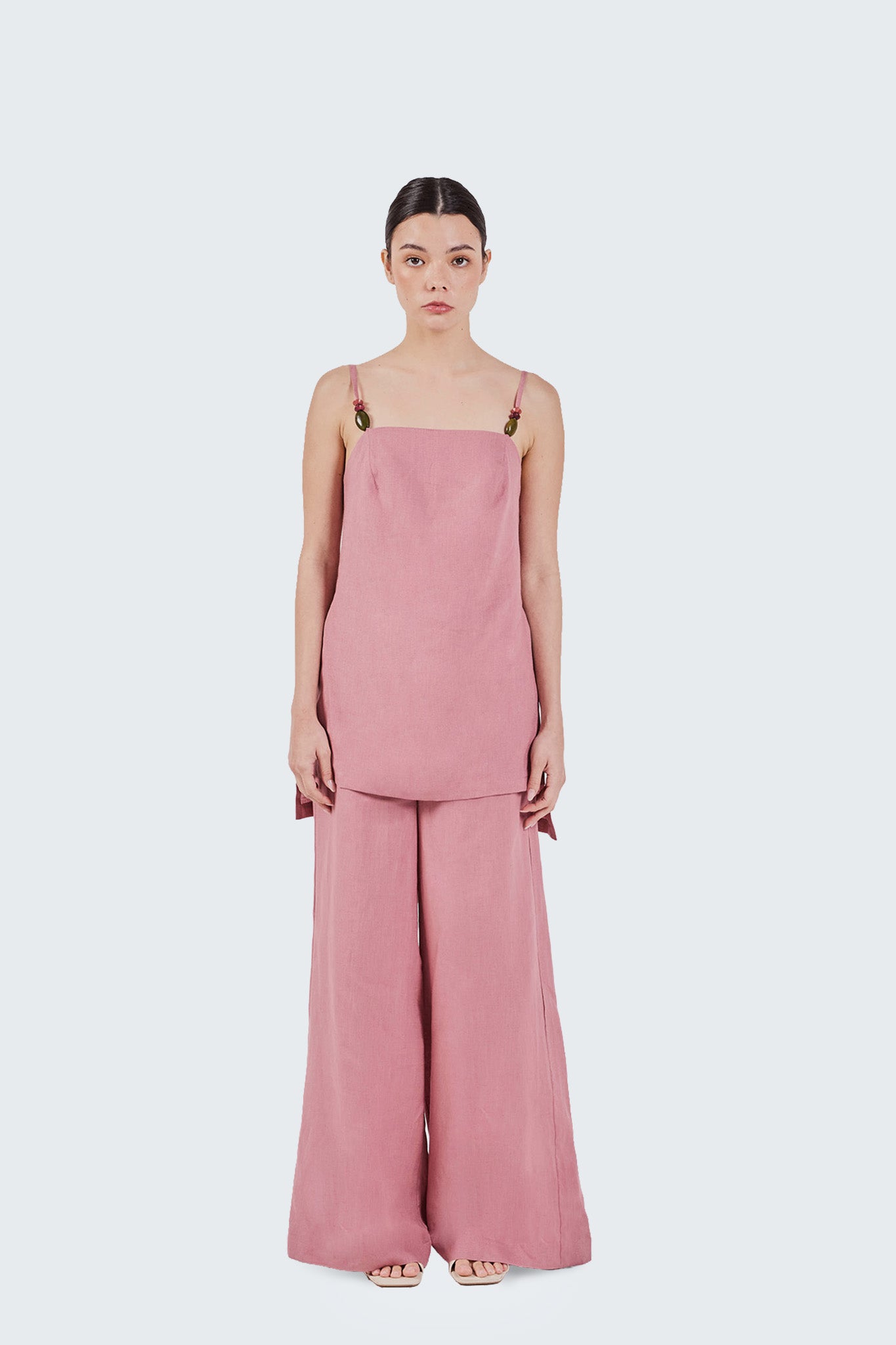 Woman wearing a pink slip blouse with wide-leg pants on a white background