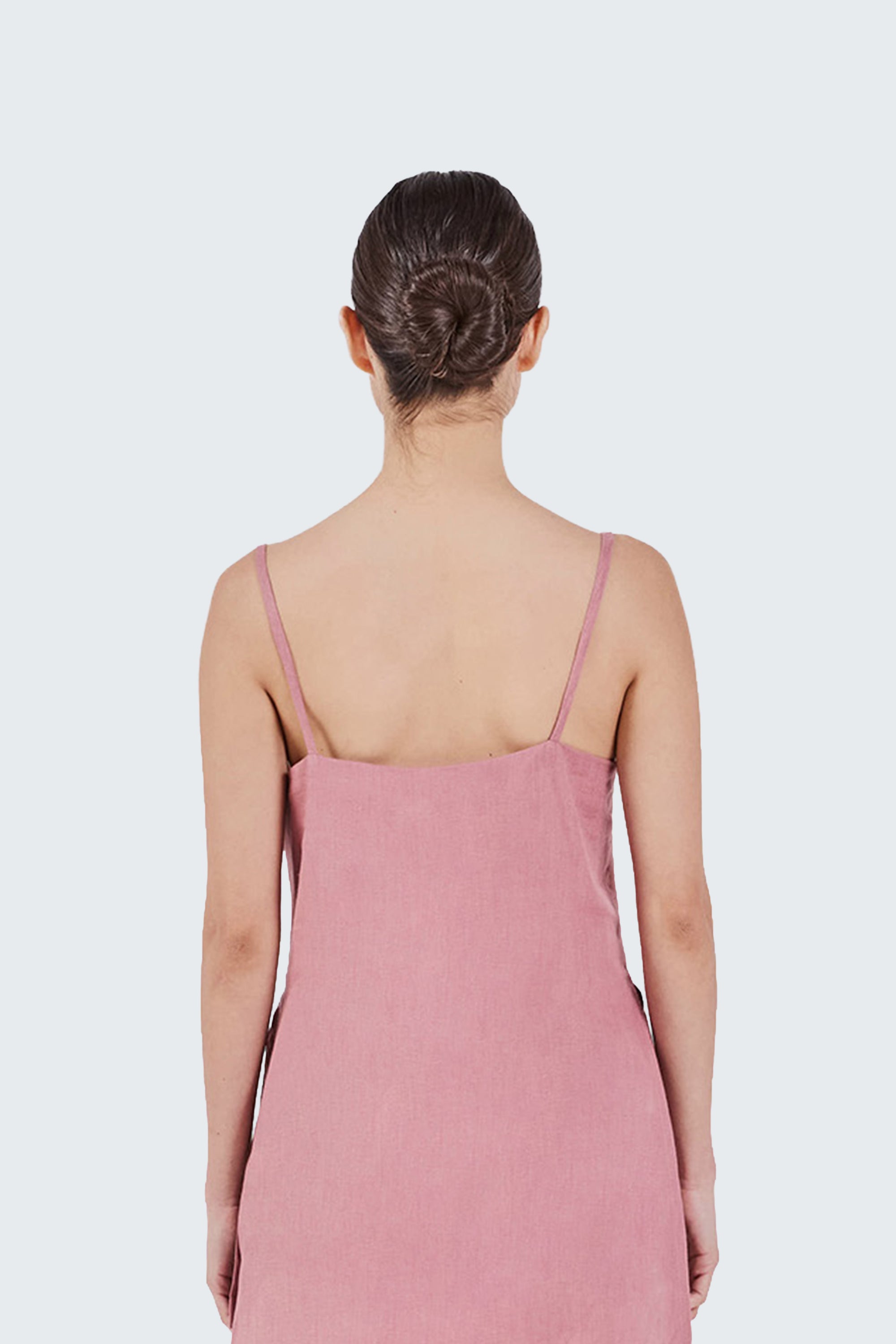 Woman back detail wearing a pink shirt with thin straps on a white background