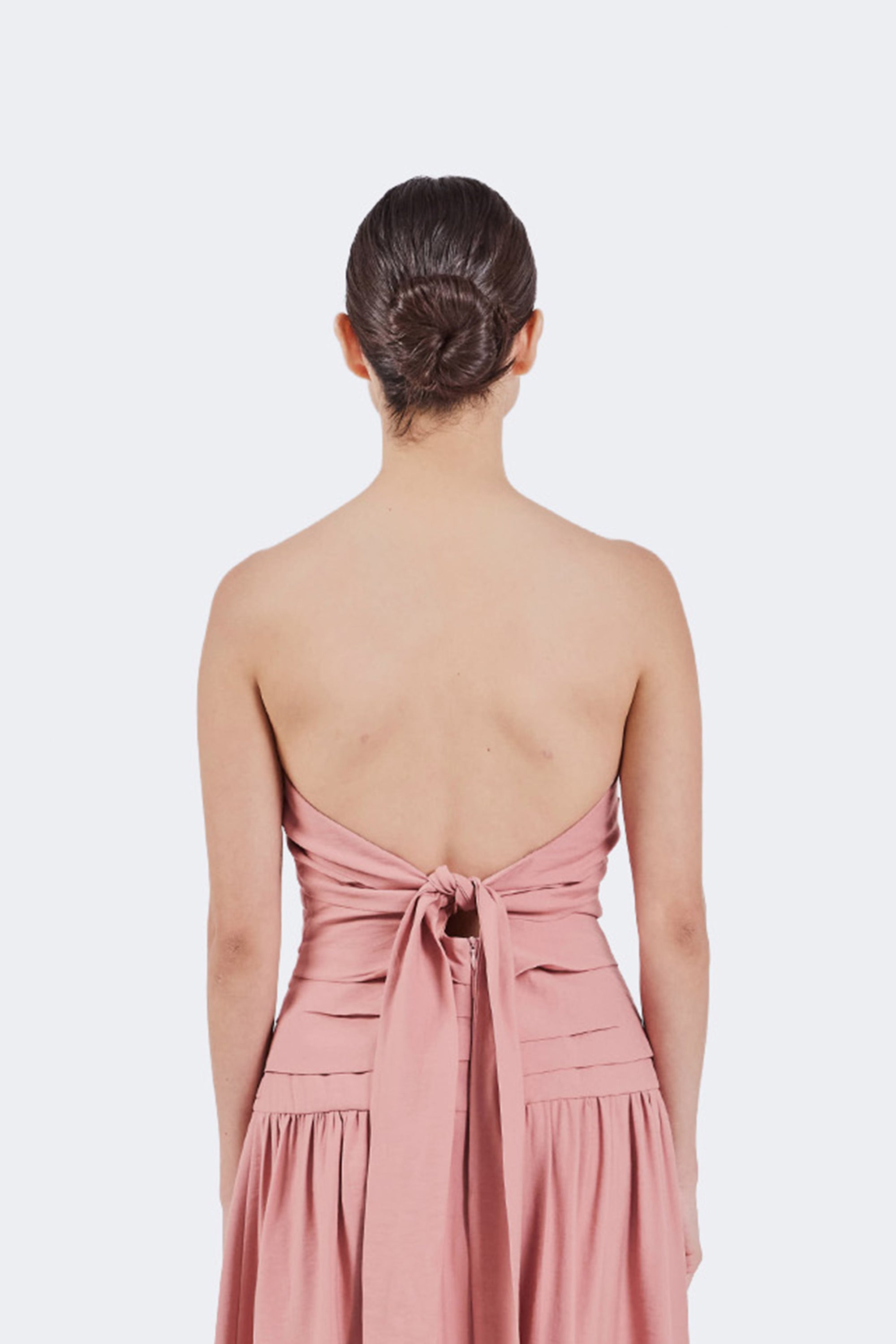 Woman wearing a pink strapless dress with a tied back on a white background