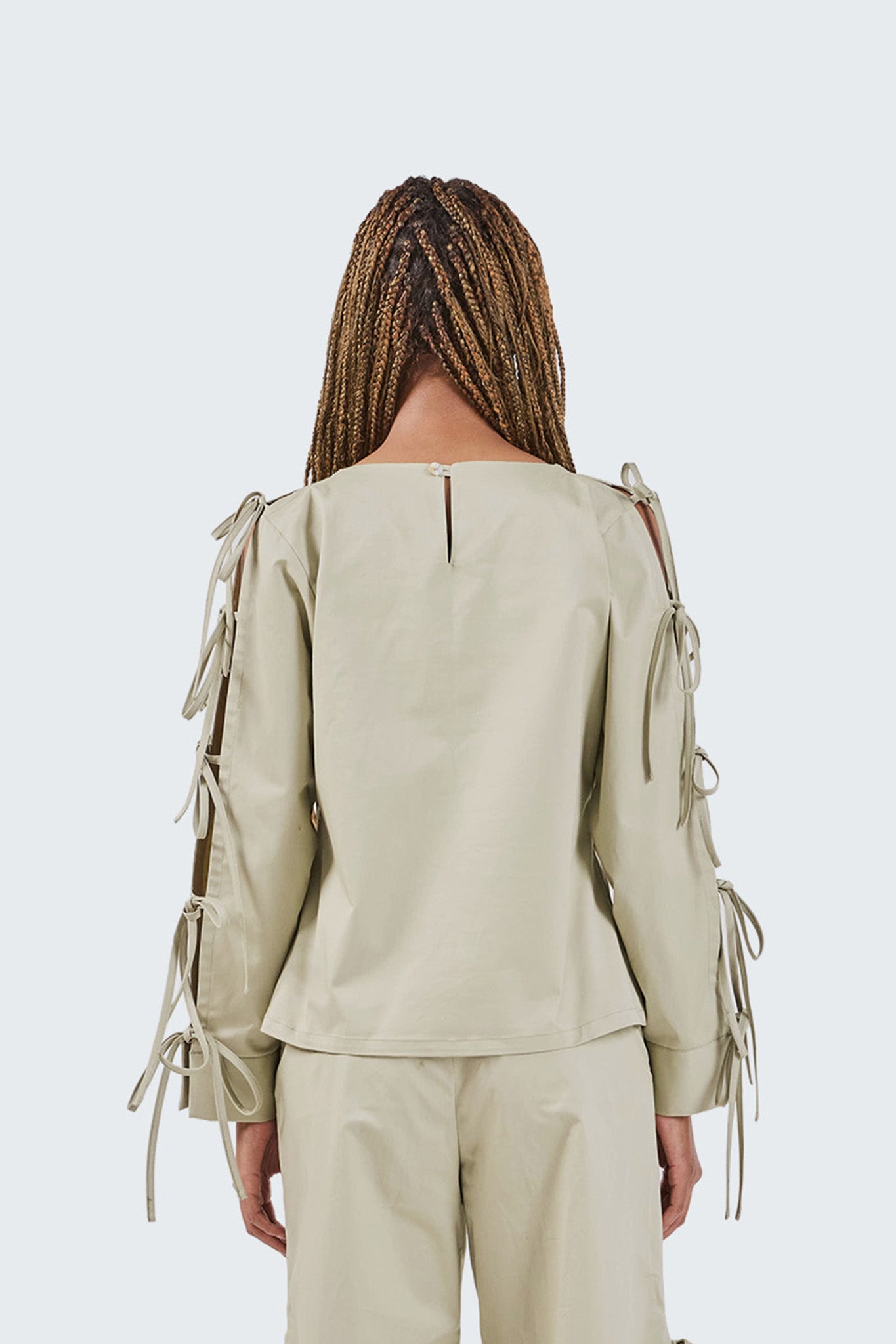Person wearing a light green outfit with lace-up sleeves on a white background