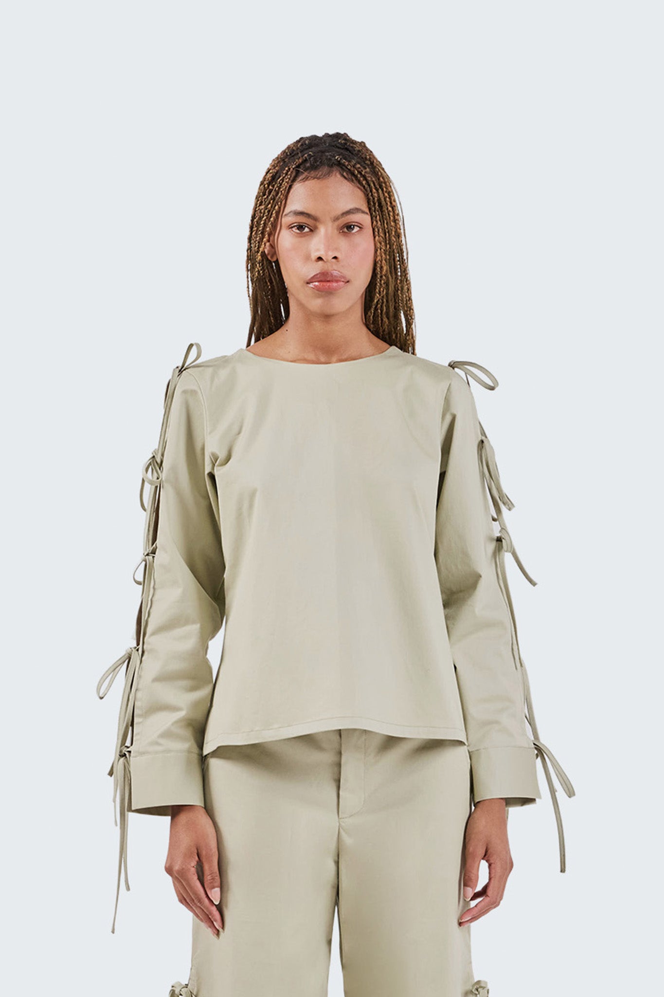 Woman wearing a beige outfit with tied sleeves on a white background