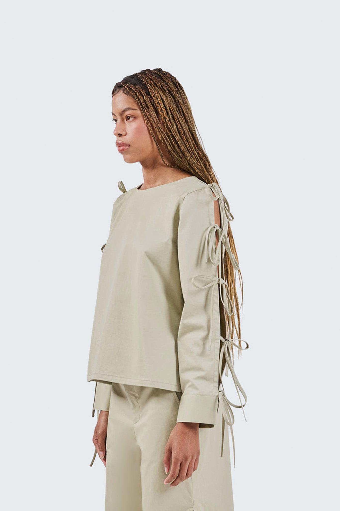 Person wearing a light green outfit with fringe details on a white background