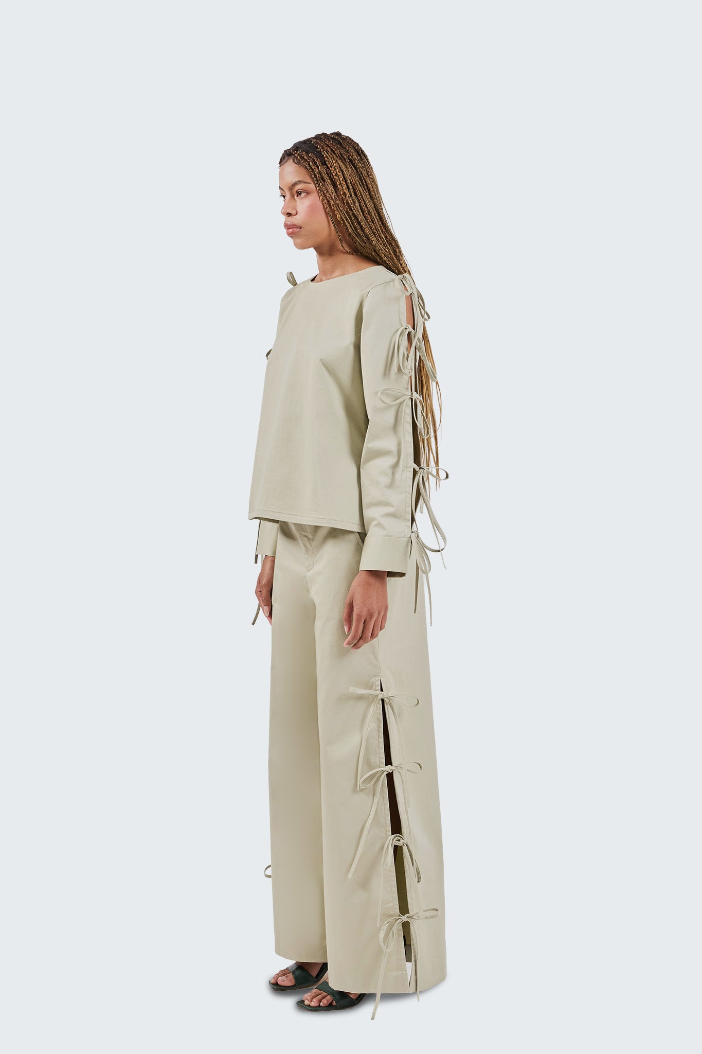 Woman wearing a baby moss outfit with lace-up details on a white background
