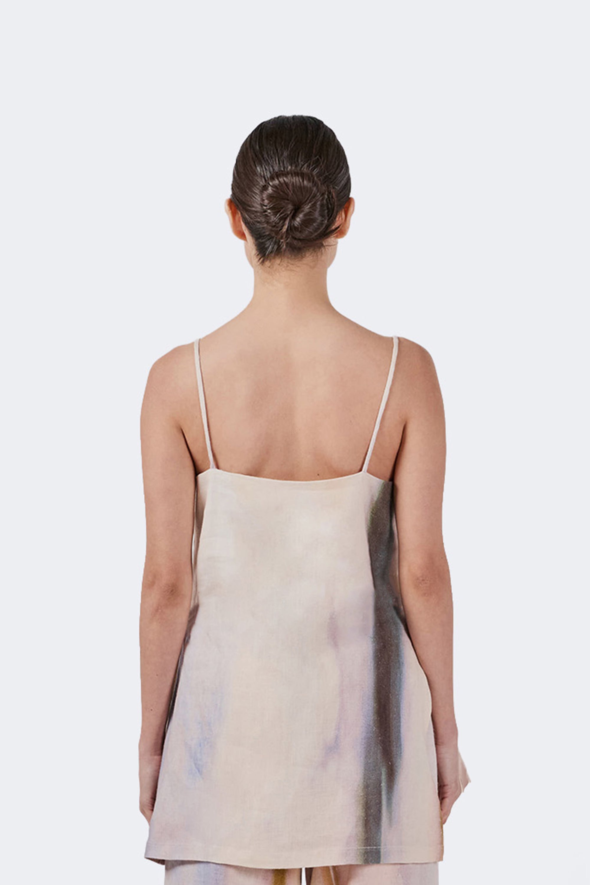 Woman wearing a beige sleeveless shirt with thin straps on a white background