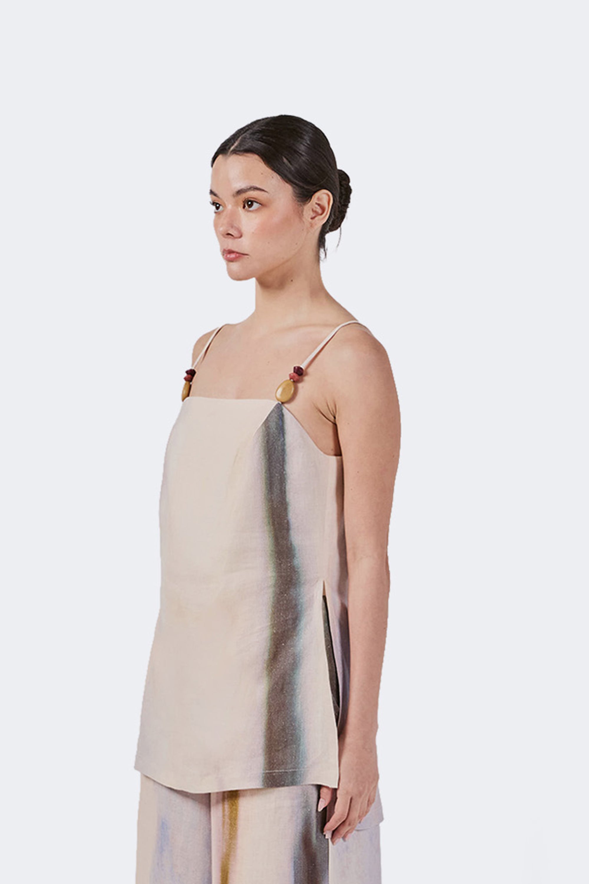 Woman wearing a beige sleeveless top with tagua detail on the strap.