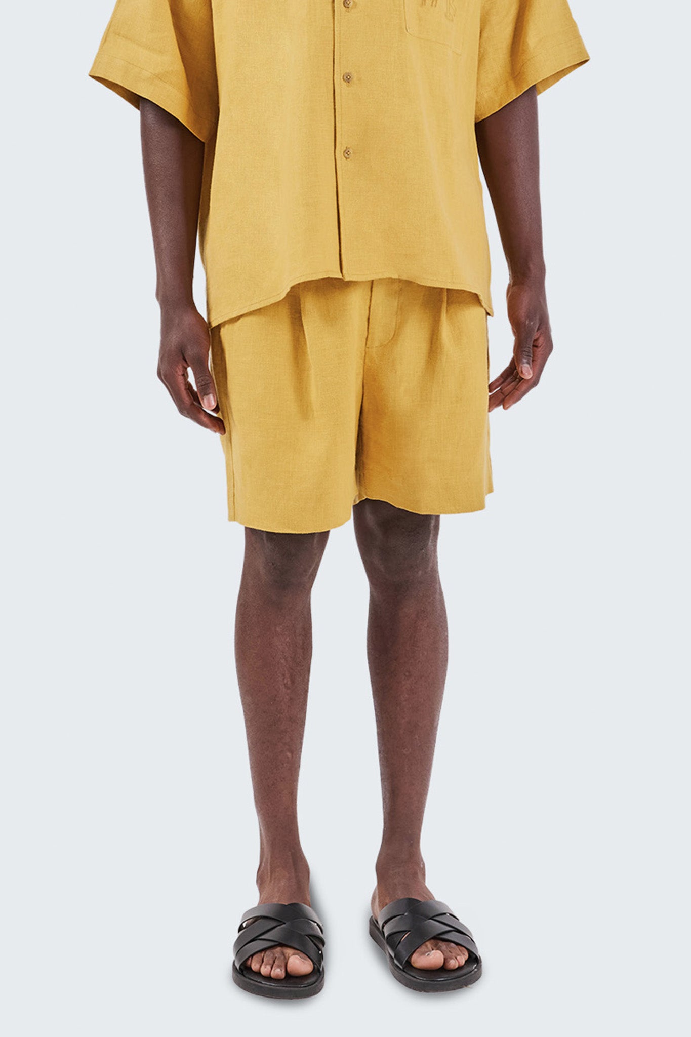 Person wearing a mustard yellow outfit with shorts and sandals on a white background