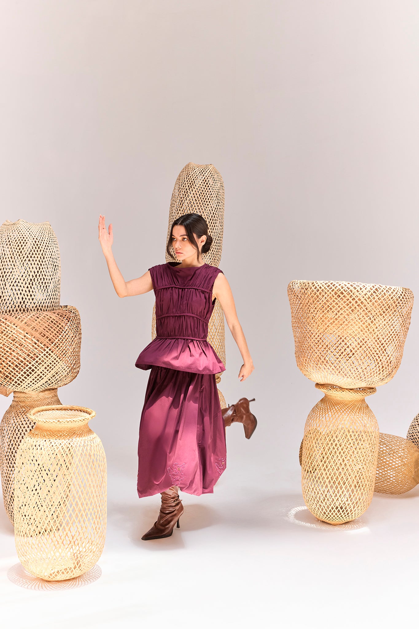Editorial campaign featuring the Palo Santo Gathered Blouse in Grape styled with the coordinating gathered skirt and leather boots, photographed among handcrafted woven sculptures inspired by Ecuadorian craftsmanship.