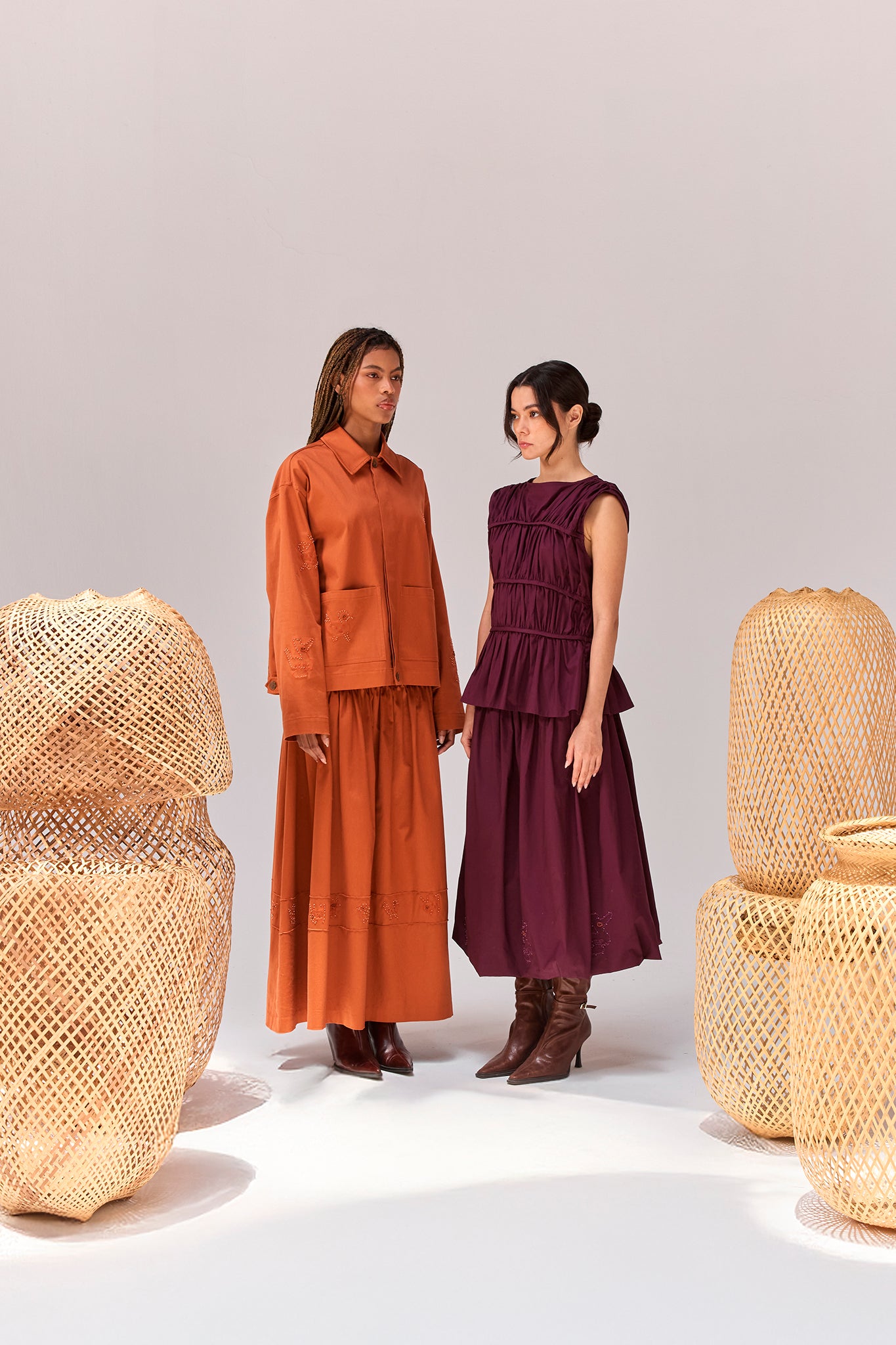 Editorial image featuring the Palo Santo Gathered Blouse in Grape styled with the coordinating skirt alongside the Payla Workman Jacket and matching skirt in Brick, photographed among handcrafted woven installations.