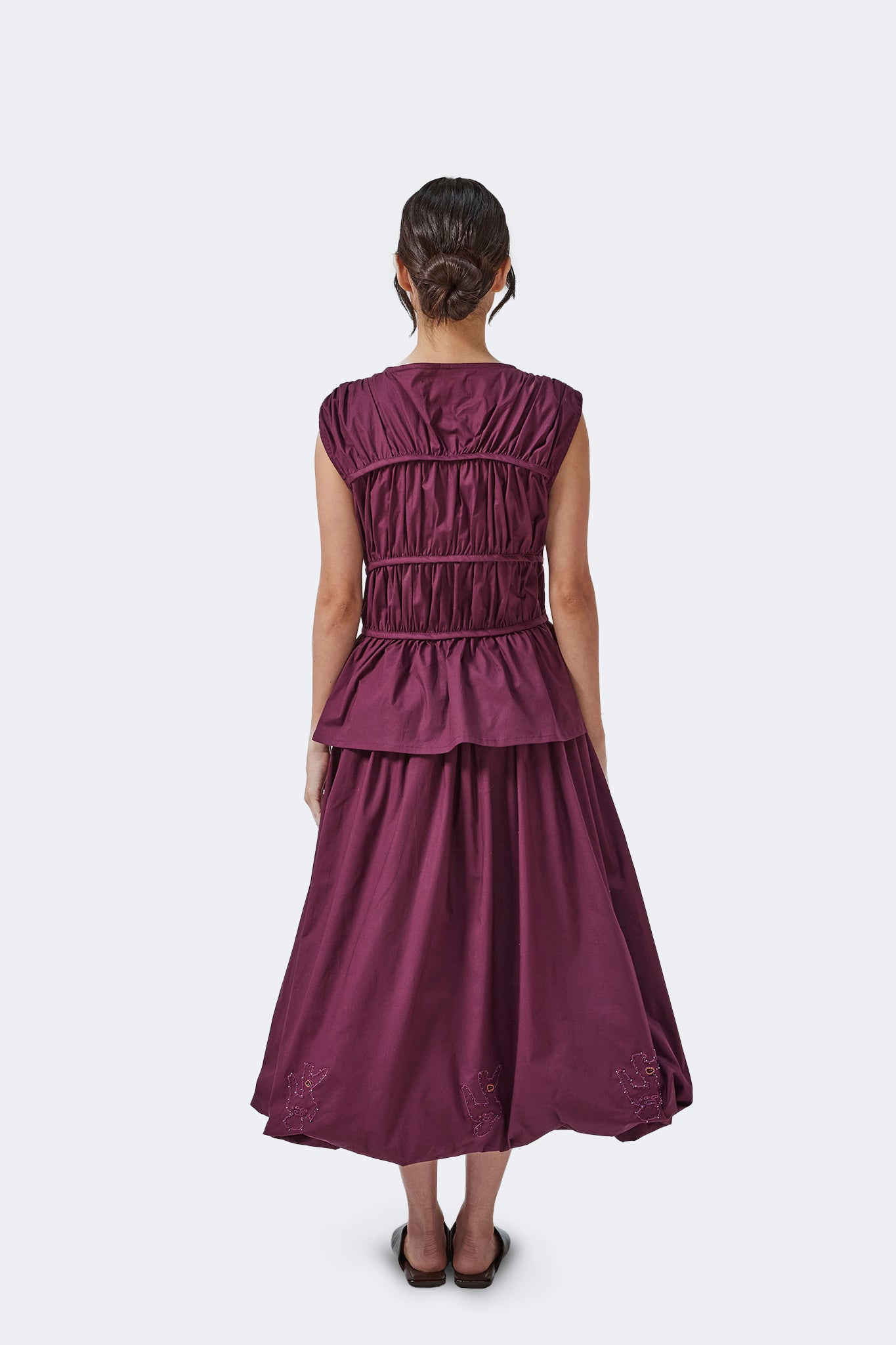 Back view of the Palo Santo Gathered Blouse in Grape paired with the coordinating gathered skirt, showcasing the sculptural panel construction and peplum hem.