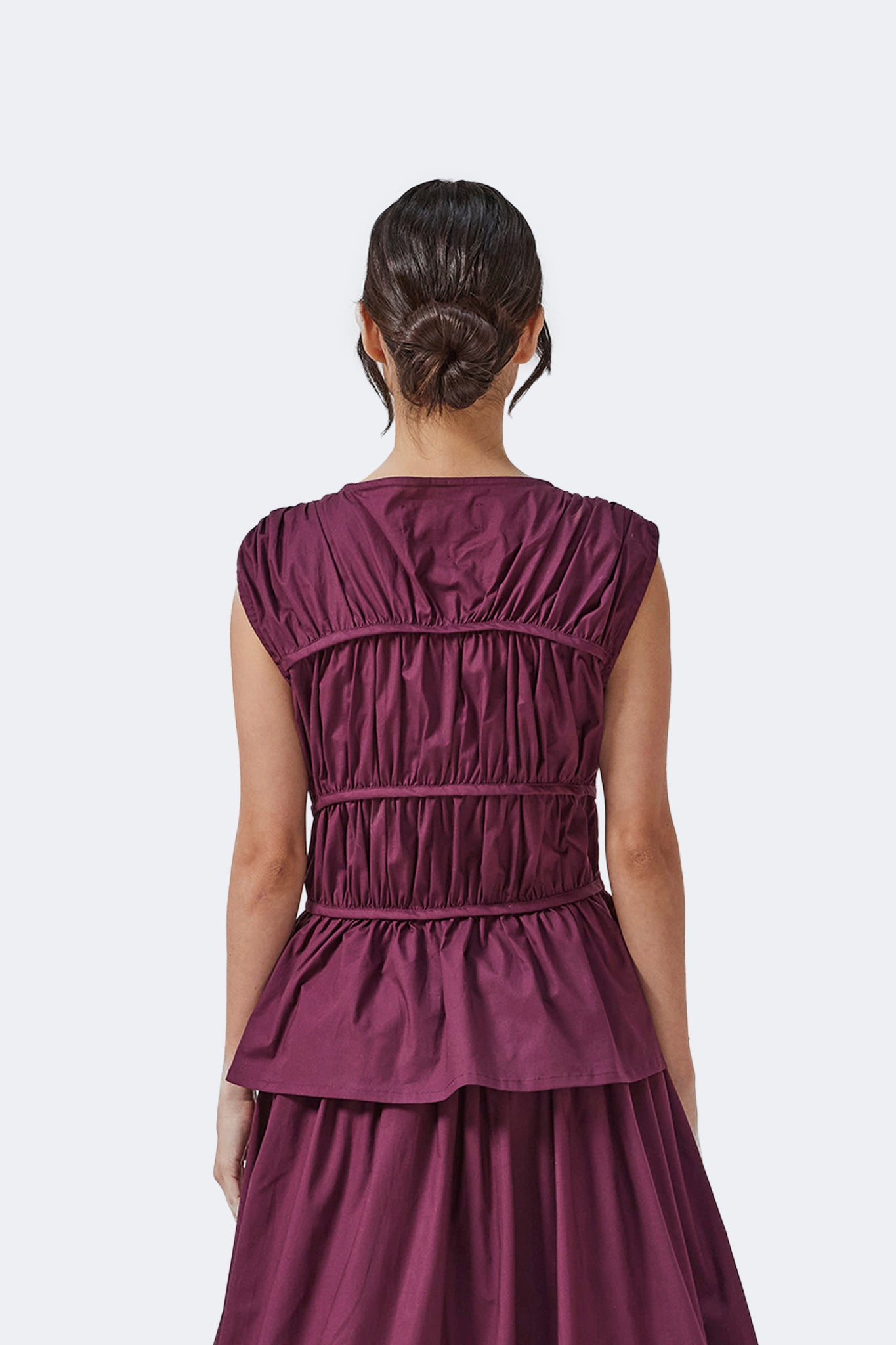 Back detail of the Palo Santo Gathered Blouse in Grape featuring sculptural gathered panels, extended cap sleeves, and a softly structured peplum silhouette.