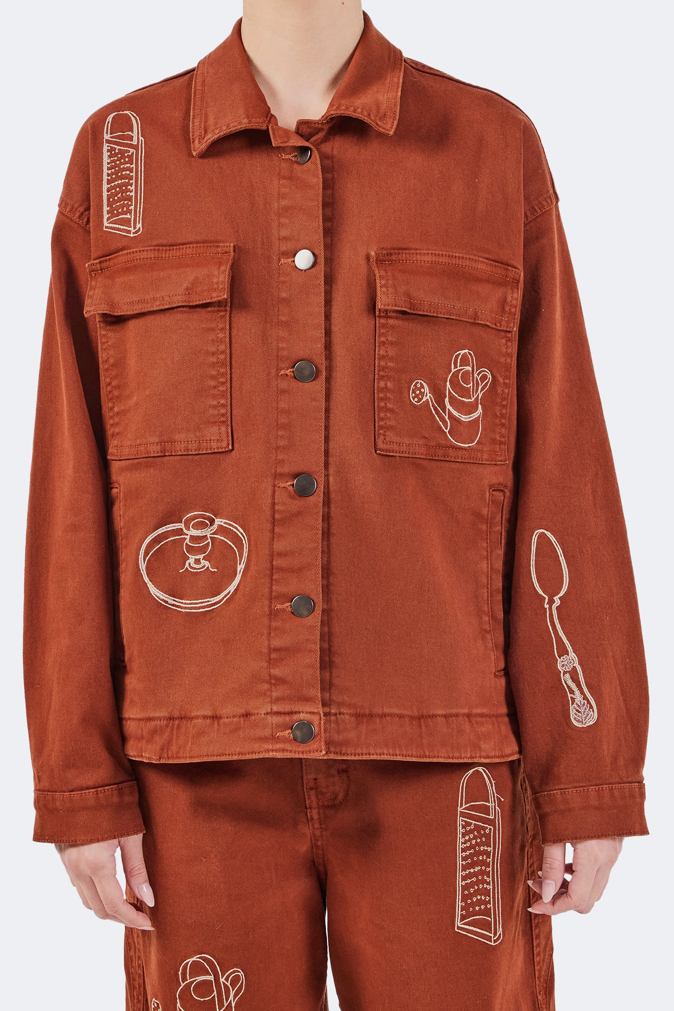Close-up of the Payla Workman Jacket highlighting oversized utility pockets, metal button closure, and embroidered motifs inspired by the Olga Fisch archive.