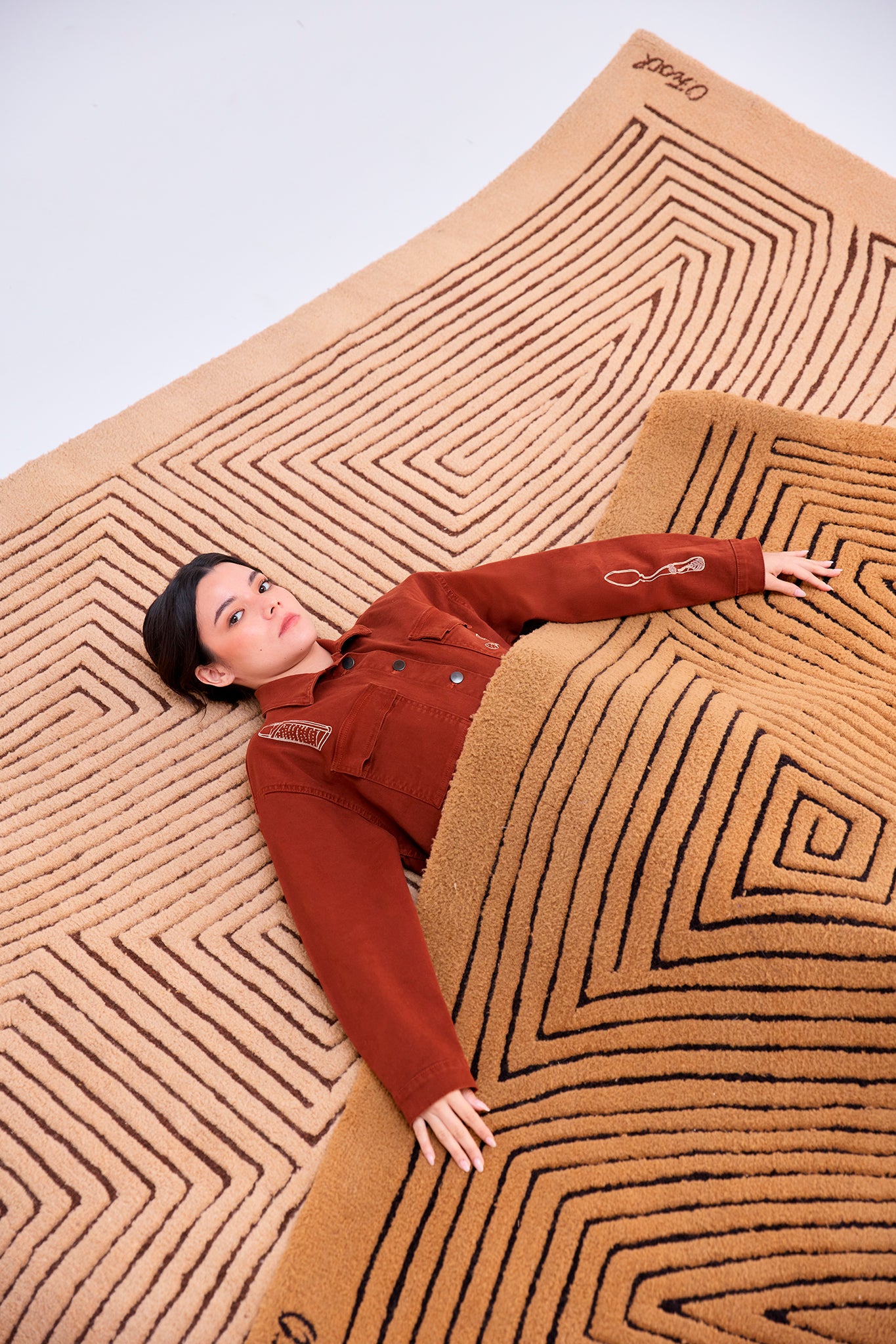 Payla Workman Jacket in Brick cotton denim featuring oversized pockets and embroidered details, photographed on handcrafted geometric rugs.