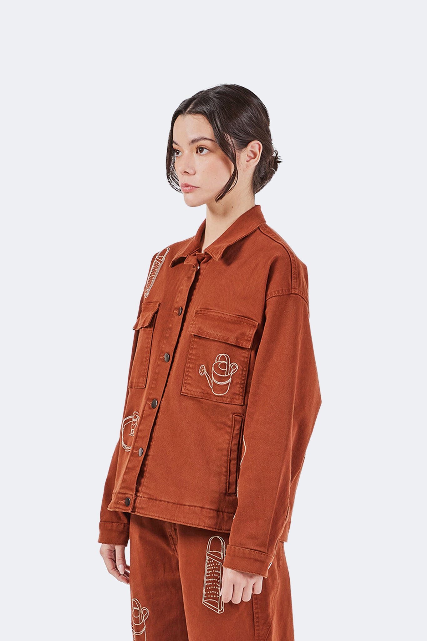 Side profile detail of the Payla Workman Jacket in Brick cotton denim, showcasing its structured silhouette, embroidered artwork, and relaxed fit.