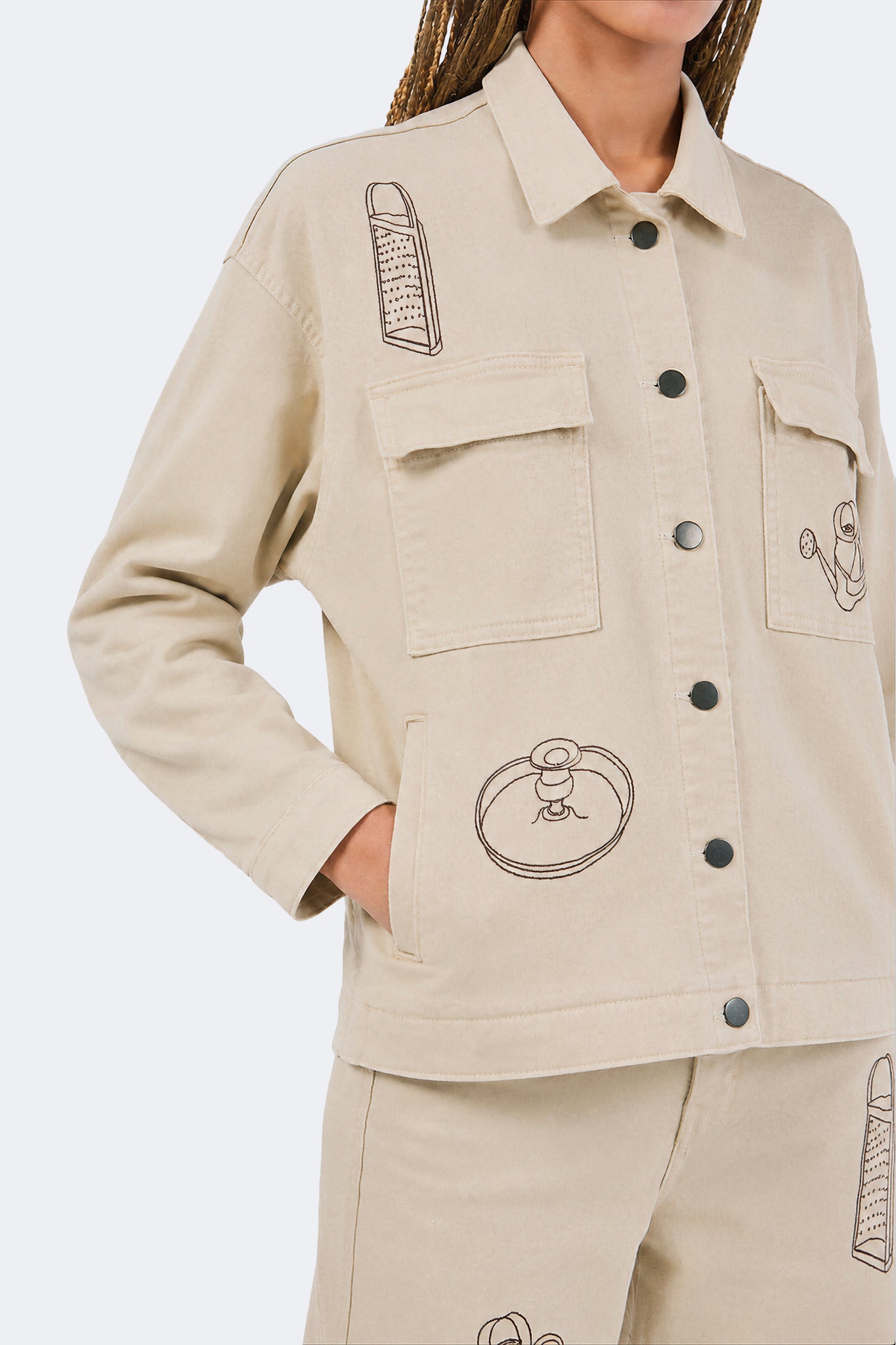 Close-up of embroidered household object motifs and utility pockets on the Payla Workman Jacket.