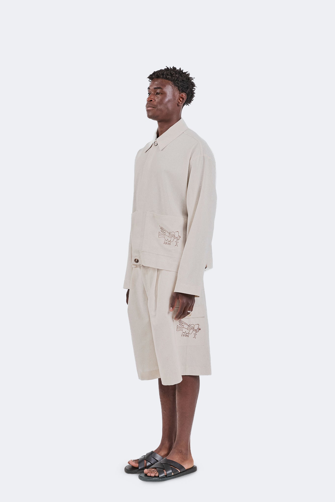 Side view of the Salango Linen Utility Jacket in Off-White highlighting the relaxed utility silhouette, natural linen fabric, oversized patch pockets, and embroidered coastal motifs.
