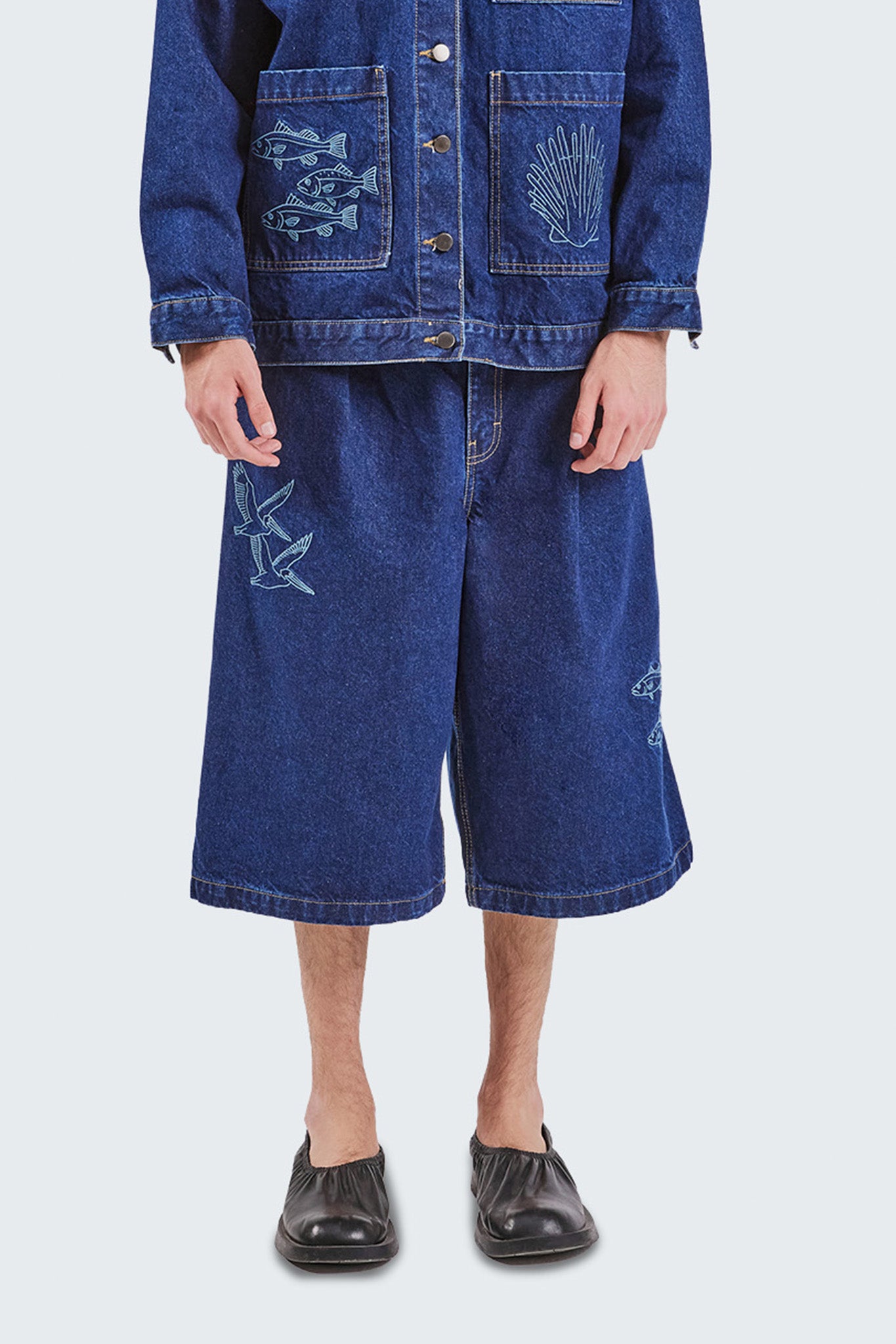 Front detail of the Salango Raw Denim Jorts highlighting embroidered seabirds, raw indigo denim texture, wide-leg silhouette, and contrast stitching.
