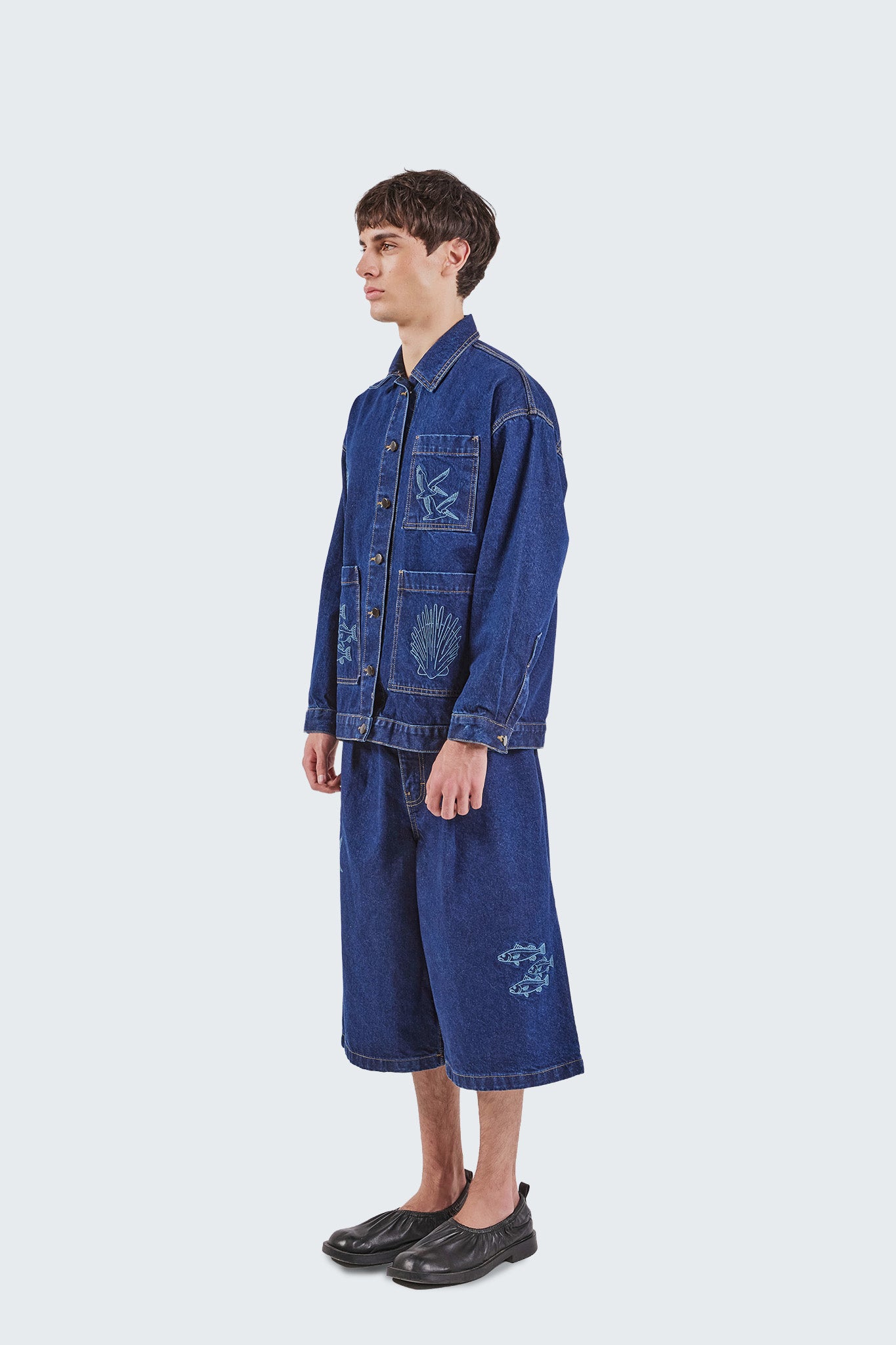 Side view of the Salango Raw Denim Jorts in indigo denim featuring a relaxed wide-leg silhouette, marine-inspired fish embroidery, and contrast topstitching.