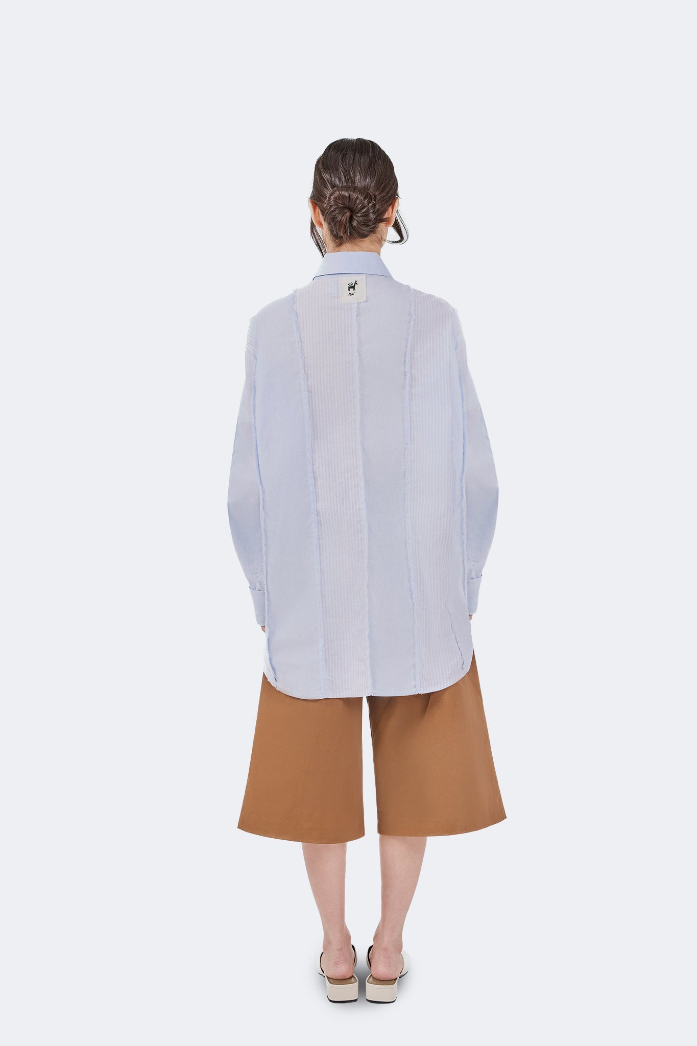 Full back view of the Salango Striped Shirt in Sky styled with wide-leg camel shorts, highlighting the relaxed fit, curved hem, and artisanal panel construction.