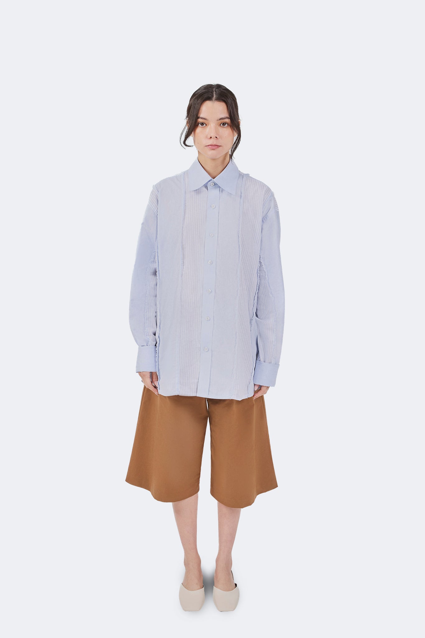 Full front view of the Salango Striped Shirt in Sky paired with wide-leg camel shorts, featuring a relaxed fit, tonal striped panels, and exposed raw-edge detailing.