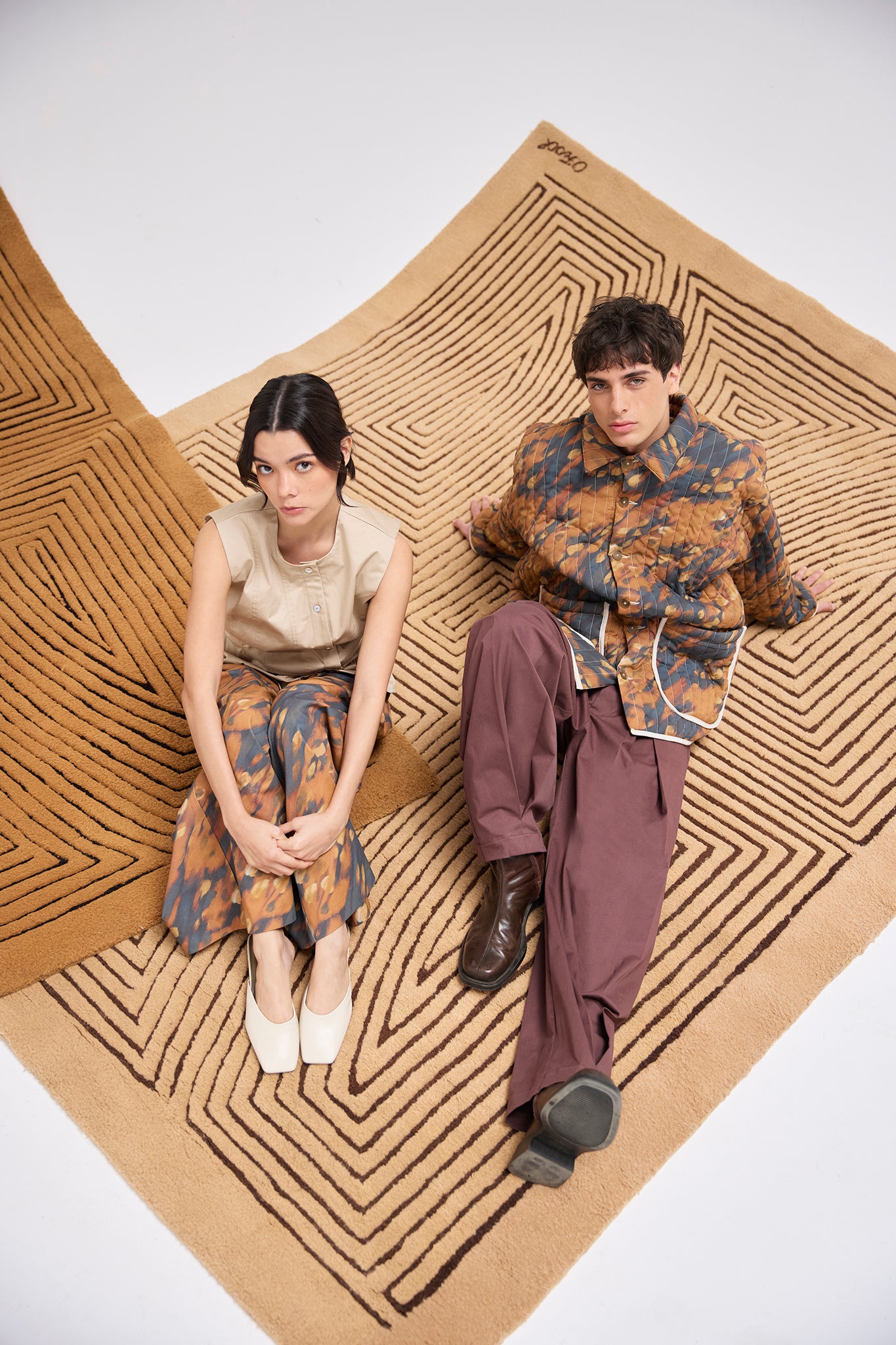 Editorial image featuring the Same Quilted Jacket paired with wide-leg trousers alongside a coordinating womenswear look on handcrafted Olga Fisch rugs.