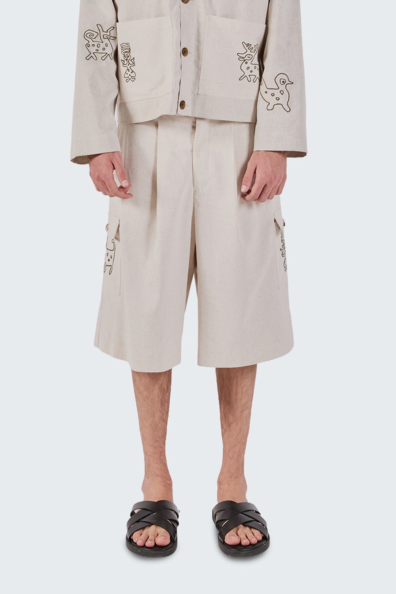 Person wearing a beige embroidered jacket and wide-leg pants on a white background