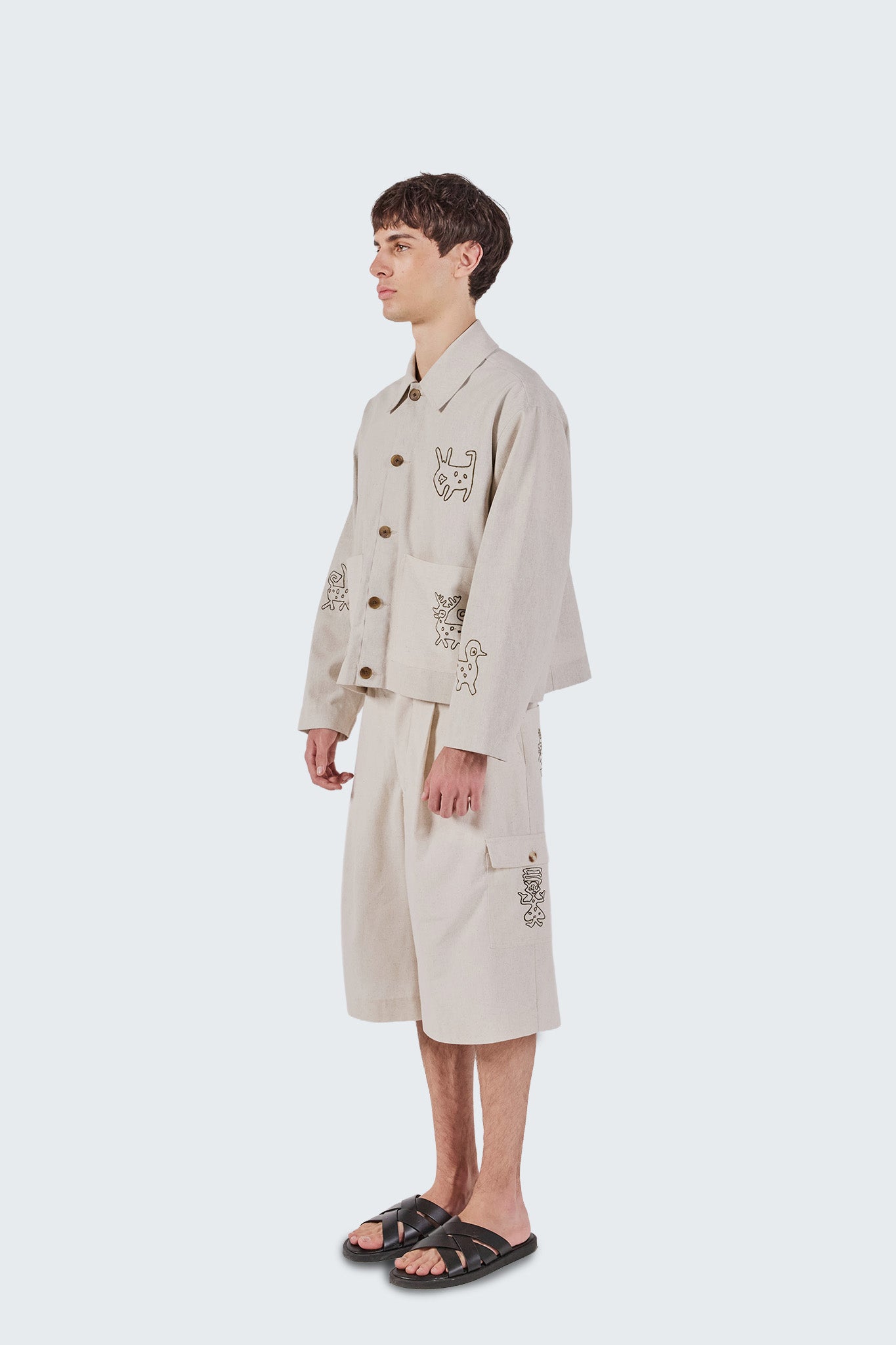 Person wearing a beige trench coat with embroidered designs on a white background