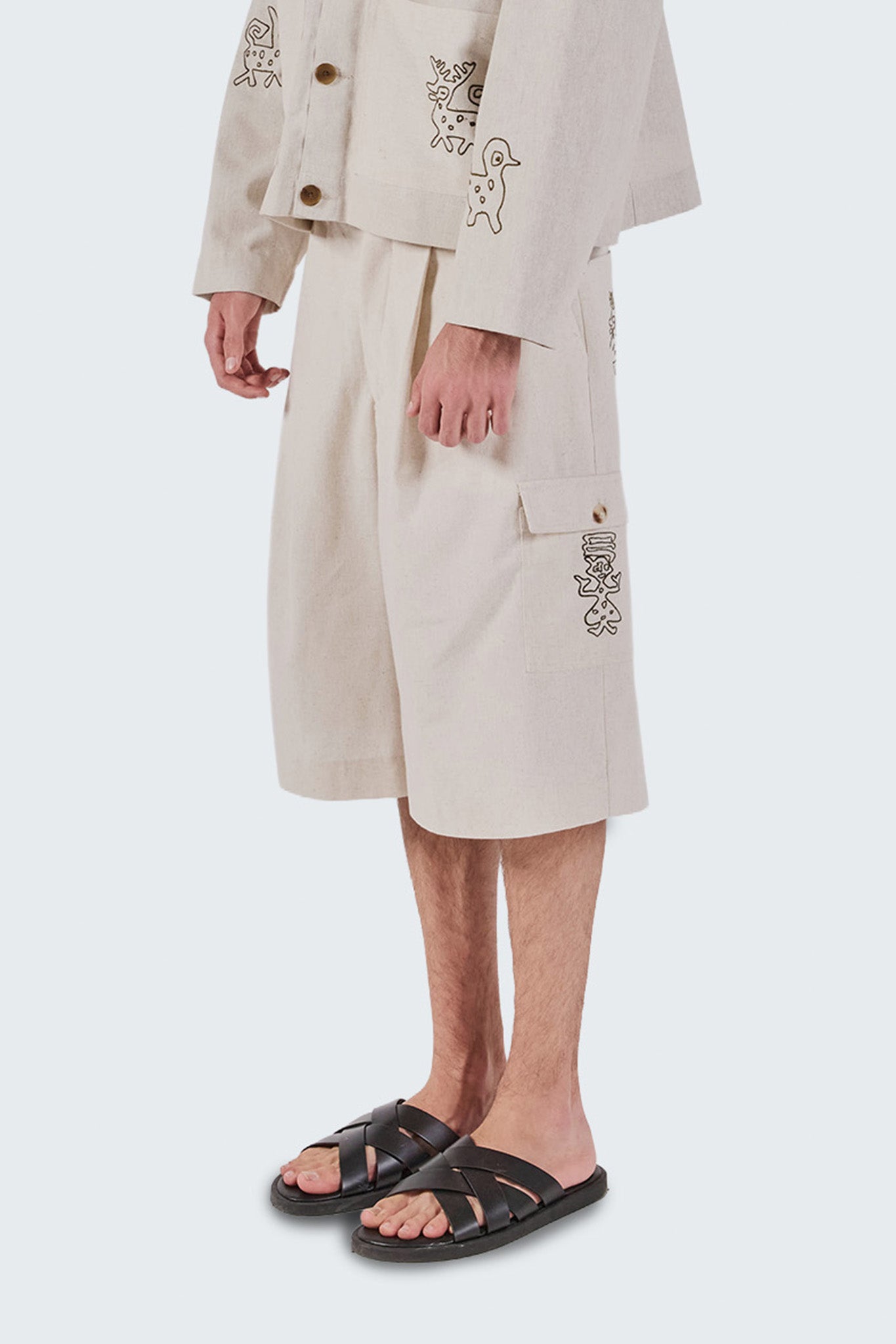 Person wearing a beige trench coat with floral embroidery on a white background
