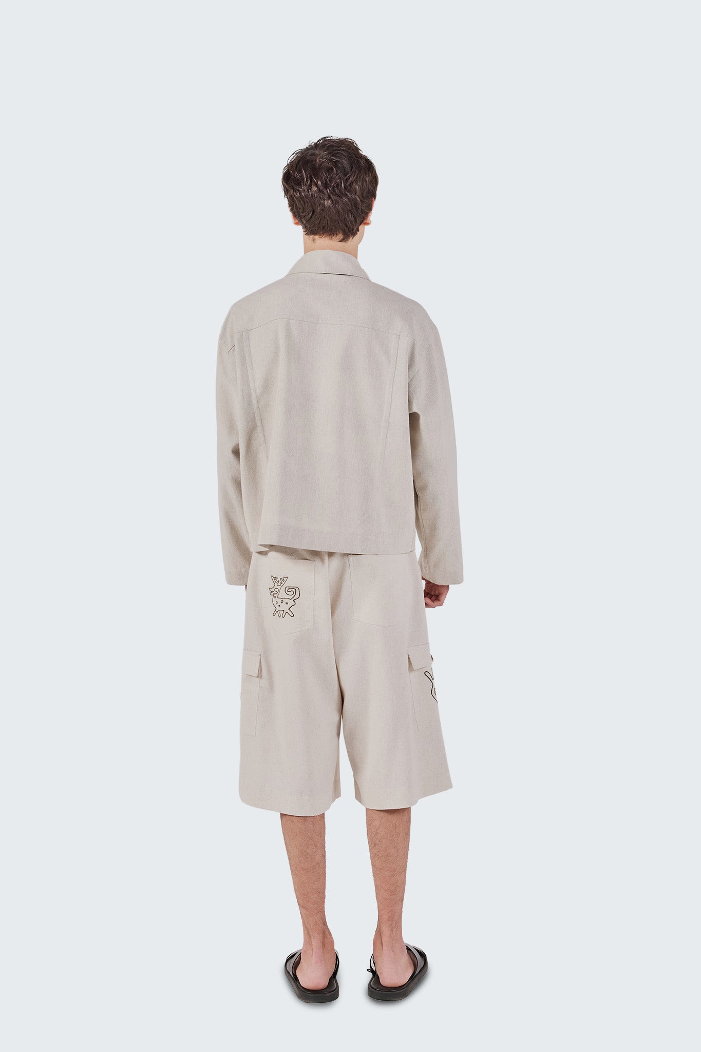 Person wearing a beige outfit with a shirt and shorts on a white background