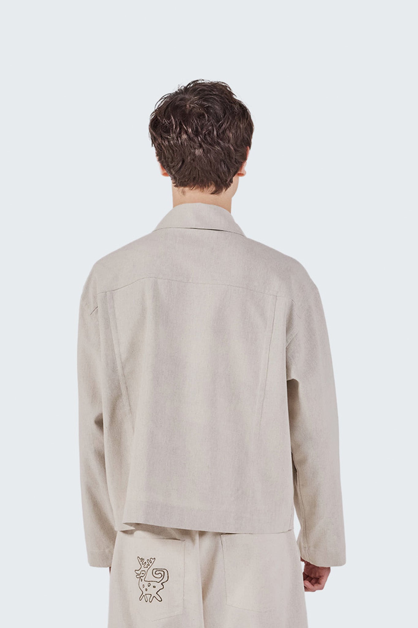 Person wearing a beige jacket and pants with a small logo on a white background