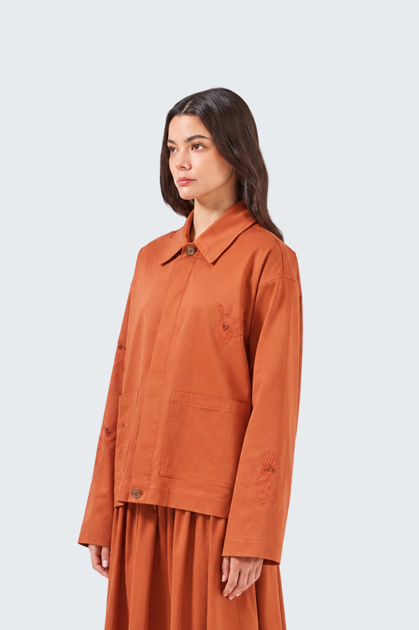 Woman wearing an orange jacket and skirt set on a light gray background