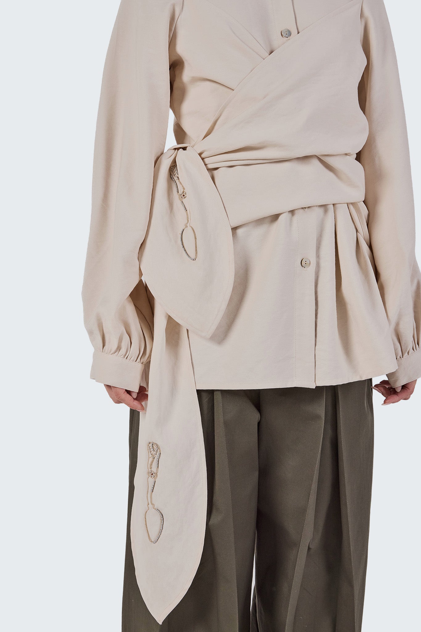 Close-up detail of the Zigze Knotted Blouse showcasing the sculptural knotted waist, embroidered sash accents, and soft cotton-viscose fabric.